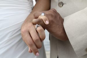 Up close shot of a wedding ring on a white female's hand and a wedding band on an Indian man's hand as the two newly weds hold hands and cross pinky fingers.